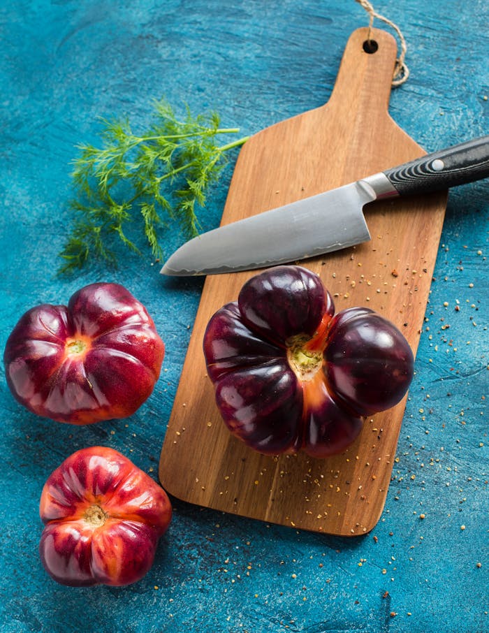 Vibrant heirloom tomatoes with herbs and knife on a wooden board, perfect for food preparation visuals.