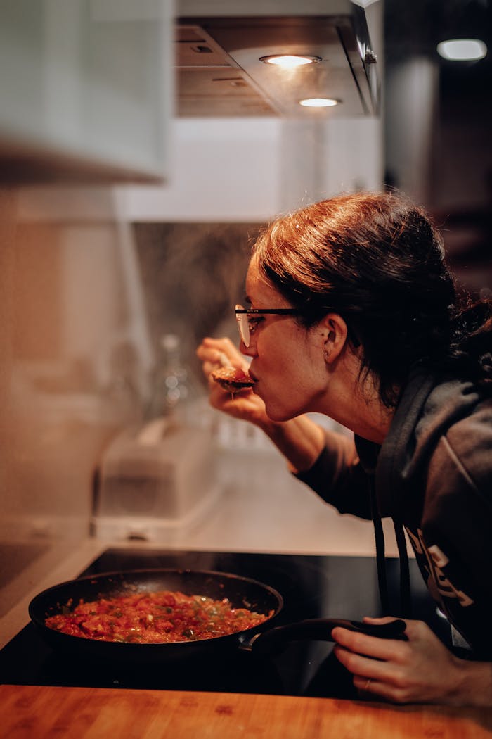 Woman cooking and tasting a dish on the stove, showcasing home culinary expertise.